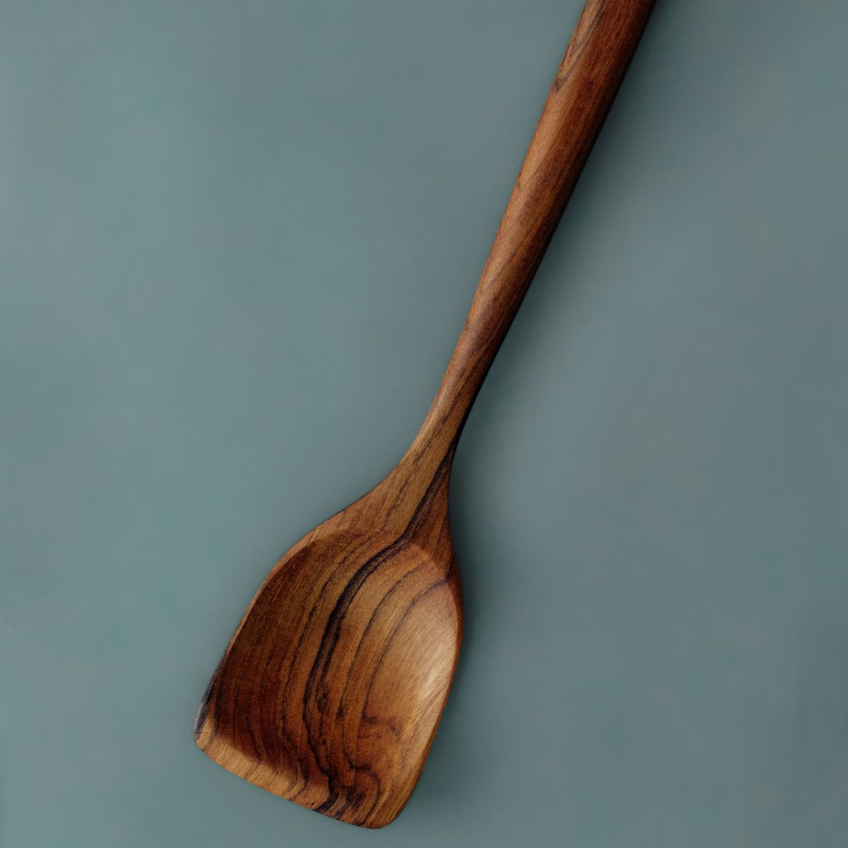 An angled view showcasing the long handle and rich timber grain of our 38cm heavy-duty teak spatula. Hand-carved from a single piece of dense teak wood, the extended length provides excellent reach and leverage for deep stockpots, large woks, and heavy cookware, keeping hands comfortably clear of heat while protecting pan surfaces.