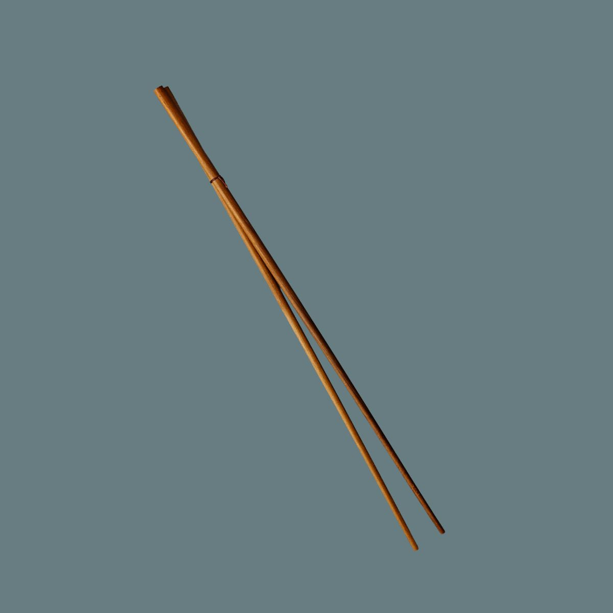 A pair of light brown very long wooden chopsticks positioned diagonally on a solid slate gray background.