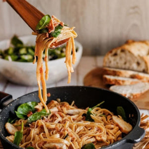 Pasta with chicken and spinach being lifted with our angled Teak spatula, served with bread and salad in the background.