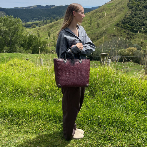 A hand-woven Krajood sea grass tote bag featuring a beautiful three-tone gradient of natural tan, golden yellow, and deep mahogany brown, finished with dark leather handles and a flower-shaped toggle closure.