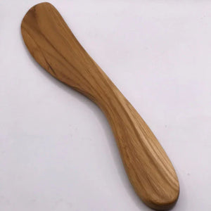 A single hand-carved spread knife made from solid teak wood, featuring an ergonomic curved handle and a broad, smooth blade ideal for serving soft cheeses, pates, and artisanal spreads.