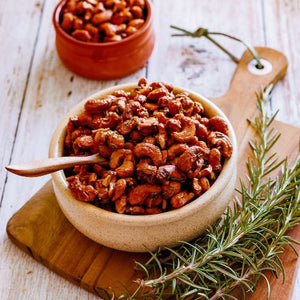 A set of artisanal teak wood teaspoons used for serving green and red chutneys in small pinch pots, pictured alongside a bowl of roasted cashews on a rustic wooden board with fresh rosemary