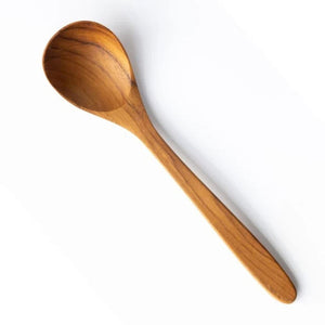A high-angle studio shot of a handcrafted 18cm teak wood soup spoon on a clean white background. The spoon features a deep, rounded bowl and a smooth, tapered handle, showcasing the rich natural golden-brown grain and organic texture of the wood.