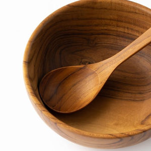 A close-up top-down view of a handcrafted teak wood soup spoon resting inside a matching solid teak bowl, showcasing the intricate natural wood grain and smooth, food-safe finish against a clean white background.