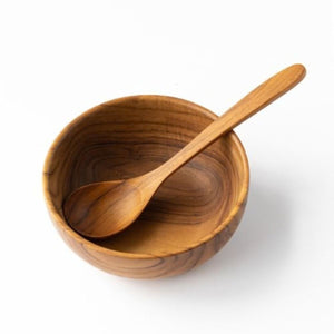 A top-down product shot of a handcrafted teak wood soup spoon resting across a matching solid teak bowl, showcasing the intricate natural wood grain and smooth, food-safe finish against a crisp white background.