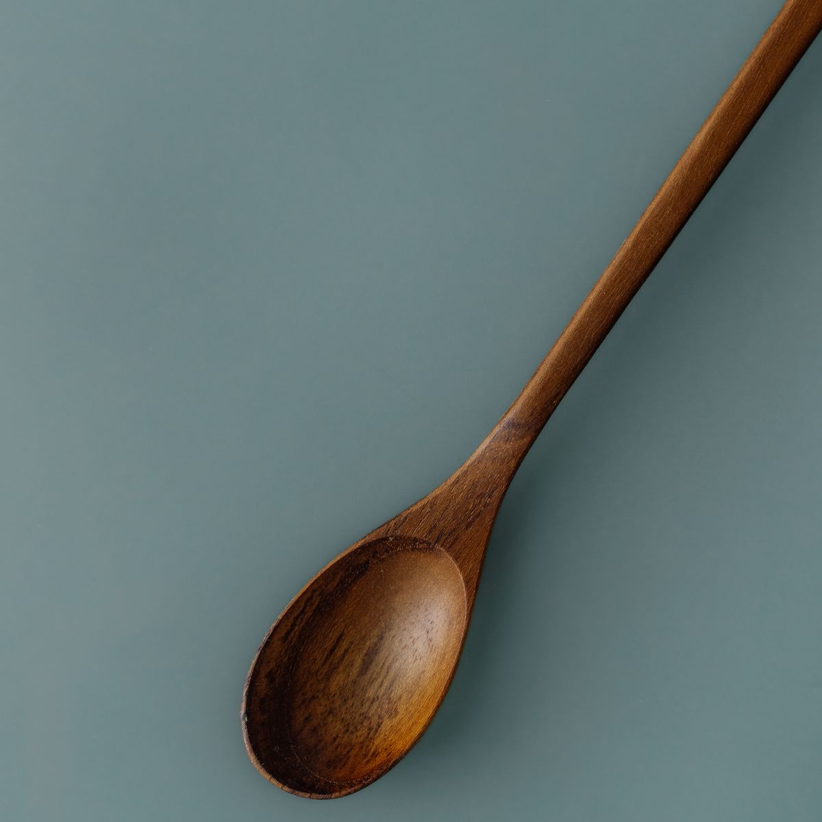 Handcrafted long-handled wooden parfait spoon made from rich teak wood by Yompai, isolated on a muted blue background