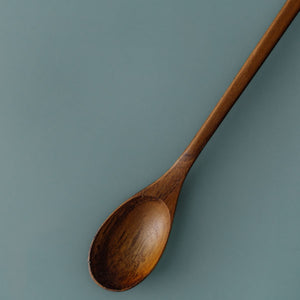 Handcrafted long-handled wooden parfait spoon made from rich teak wood by Yompai, isolated on a muted blue background