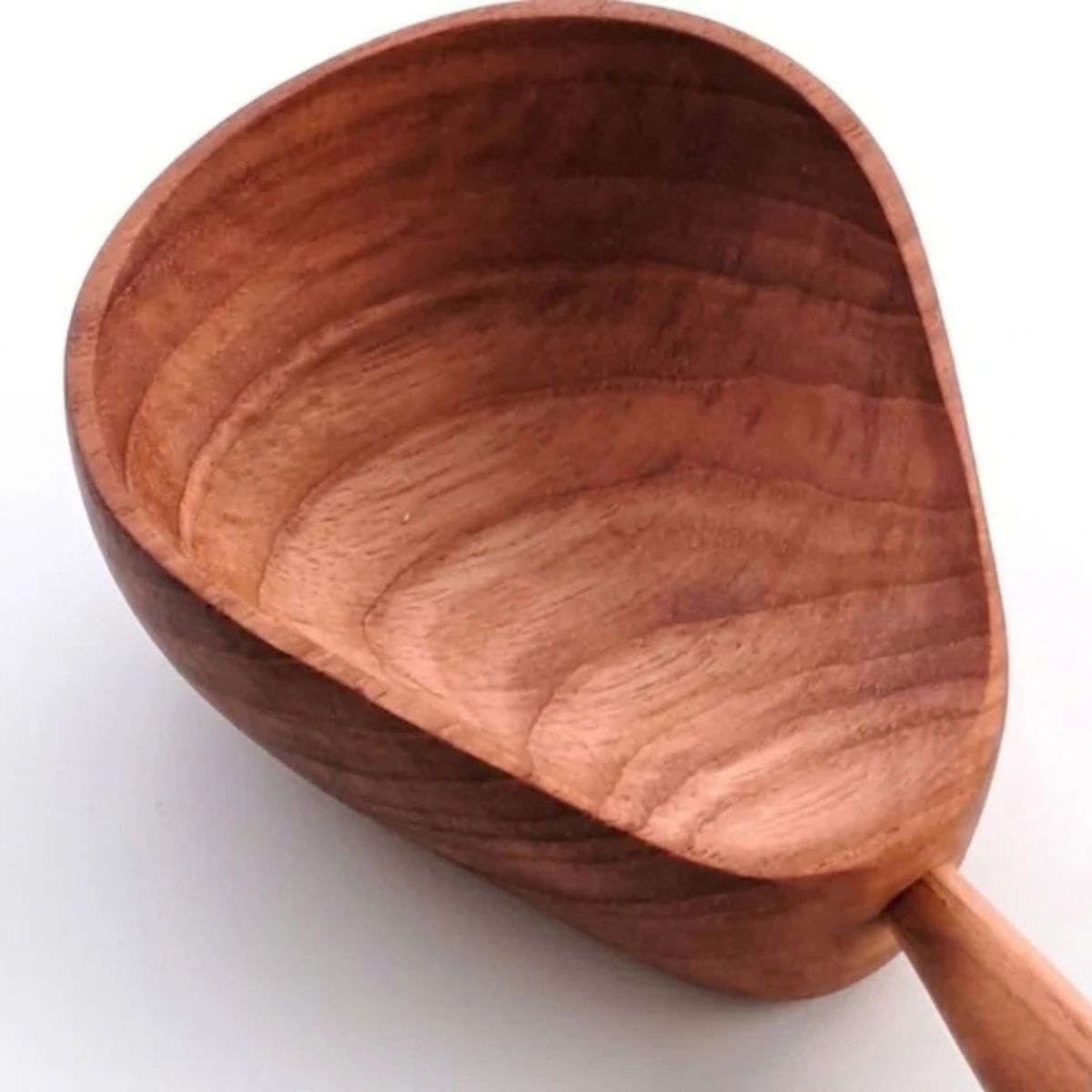An elevated, angled view of a handcrafted pear-shaped teak wood bowl with a rich natural grain, featuring a small carved handle at its base, set against a seamless, clean white background