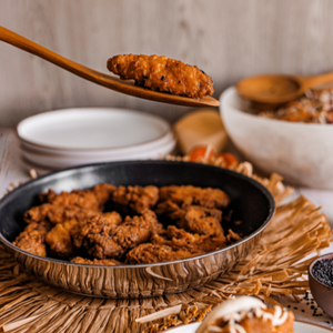a lifestyle photo of a wooden curved spatula, serving small pieces of fried meat from a frying pan.