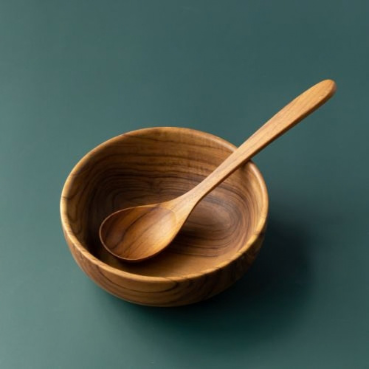 Handcrafted wooden soup spoon and wooden bowl against a green background