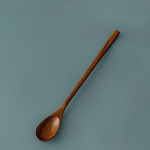 Top-down full-length view of Yompai's handcrafted long-handled wooden parfait spoon, displayed on a smooth muted blue background.