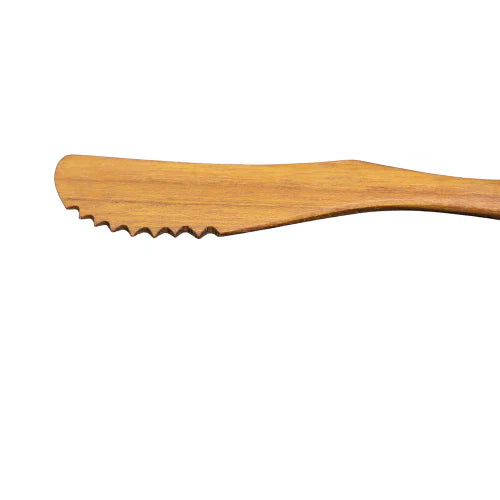 A close-up side view of a handcrafted teak wood knife, emphasizing the sharp, serrated notched blade designed for clean slicing of soft breads and gourmet cheeses.