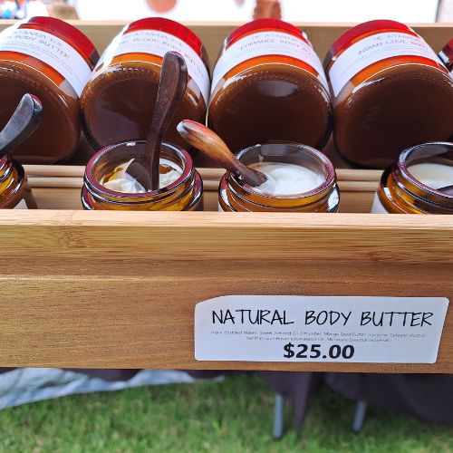 Several small, handcrafted rosewood spoons used as individual testers for natural skin balms in amber glass jars, showcasing their rich dark wood grain and ideal size for hygienic product sampling.