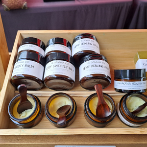 Handcrafted rosewood mini spoons used as hygienic applicators for skincare samples, showcasing their smooth finish and deep reddish-brown wood grain while resting in glass jars at a local market.