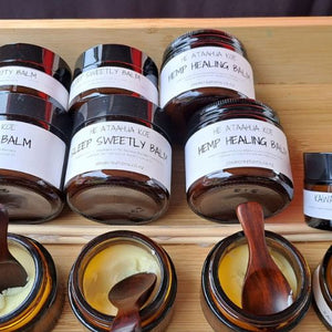 Several small handcrafted rosewood spoons used as applicators for natural skin balms in amber glass jars at a craft market, highlighting their smooth, non-toxic finish for personal care products.