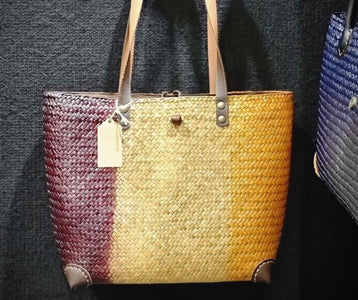 Close-up of a handcrafted three-toned woven bag made from natural sea grass, showing the high-quality burgundy and honey-colored fiber patterns and durable leather handle attachments.