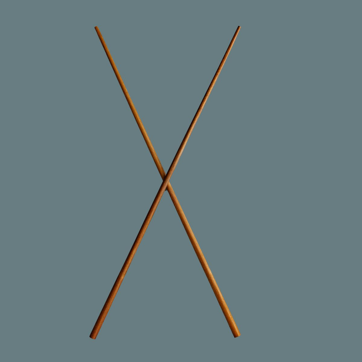 Extra long wooden cooking chopsticks crossing in an X shape against a solid slate blue-gray background.