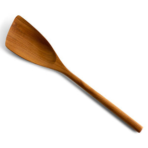 A high-angle shot of a handcrafted curved wooden spatula isolated on a crisp white background. The image highlights the ergonomic long handle and the uniquely angled, wide turner head designed for reaching into the corners of pans. The rich, golden-brown teak wood grain is clearly visible across the smooth, polished surface of the utensil, emphasizing its artisanal quality and durable construction for everyday cooking.