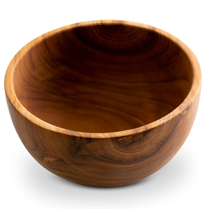 A top-down product photograph of a handcrafted everyday wooden bowl carved from sustainable teak, centered against a smooth, matte slate-grey background. The image highlights the wide, shallow profile of the bowl and its rich, golden-brown timber tones, showcasing a prominent and beautiful natural wood grain. Expertly shaped from a single piece of non-toxic, food-safe teak, this durable bowl is designed as a versatile culinary essential for serving salads, grains, or snacks.