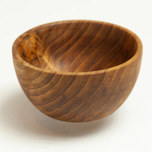 A handcrafted mini teak wood bowl, 7 cm in diameter, featuring a deep, rounded basin and a rich, swirling natural wood grain. Carved from a single piece of golden-brown teak, this small bowl has a smooth, food-safe finish and a stable base. It is the perfect sustainable size for use as a salt cellar, spice pinch pot, or for serving small garnishes in an eco-friendly, artisanal kitchen.
