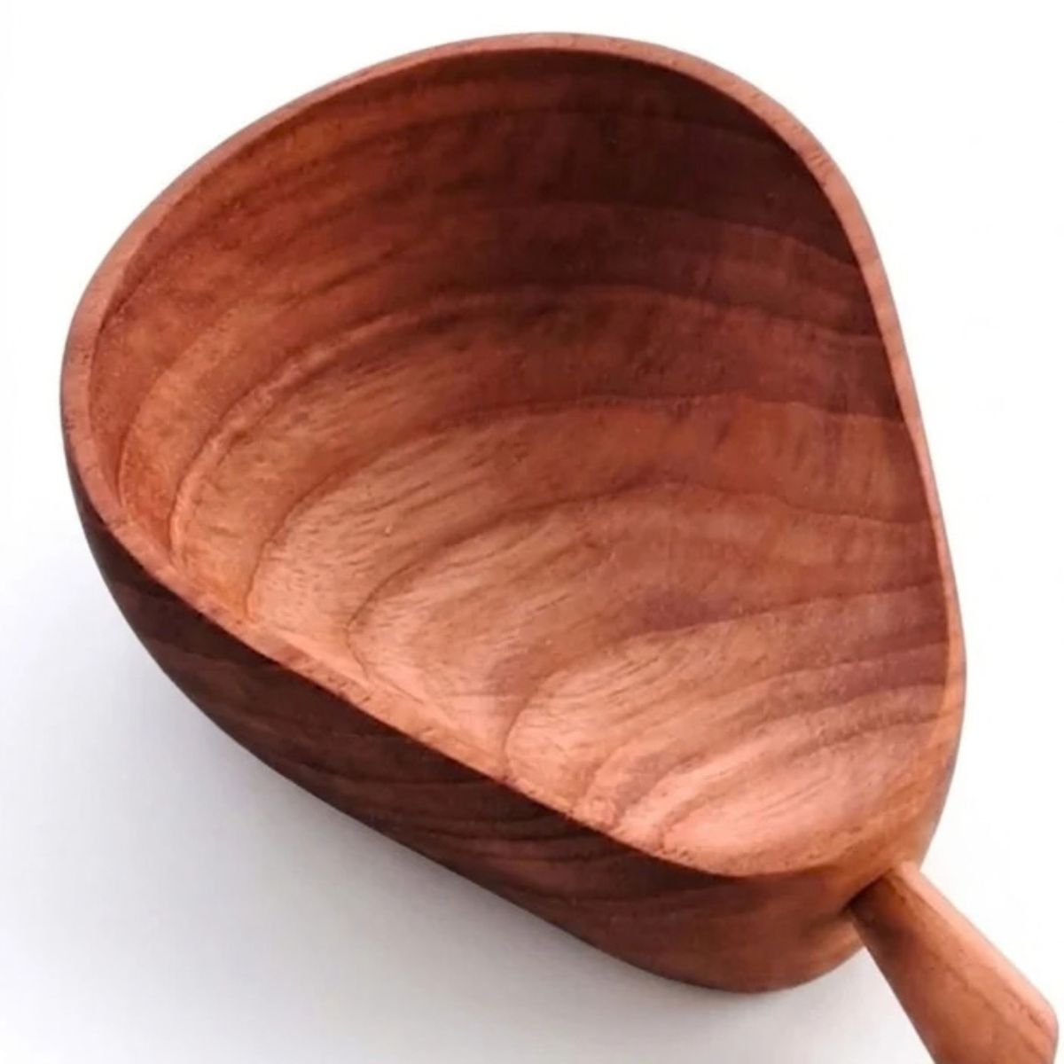A top-down product photograph of a handcrafted pear-shaped dip bowl carved from sustainable teak wood, angled diagonally against a neutral, textured grey wall surface. The 10cm long dish features a wide rounded base tapering into a narrower neck with a small, stylized wooden stem handle at the tip. The image captures the deep, smooth interior basin, highlighting the rich golden-brown timber tones and prominent, rippled natural wood grain patterns of the non-toxic, food-safe single-piece mini bowl.