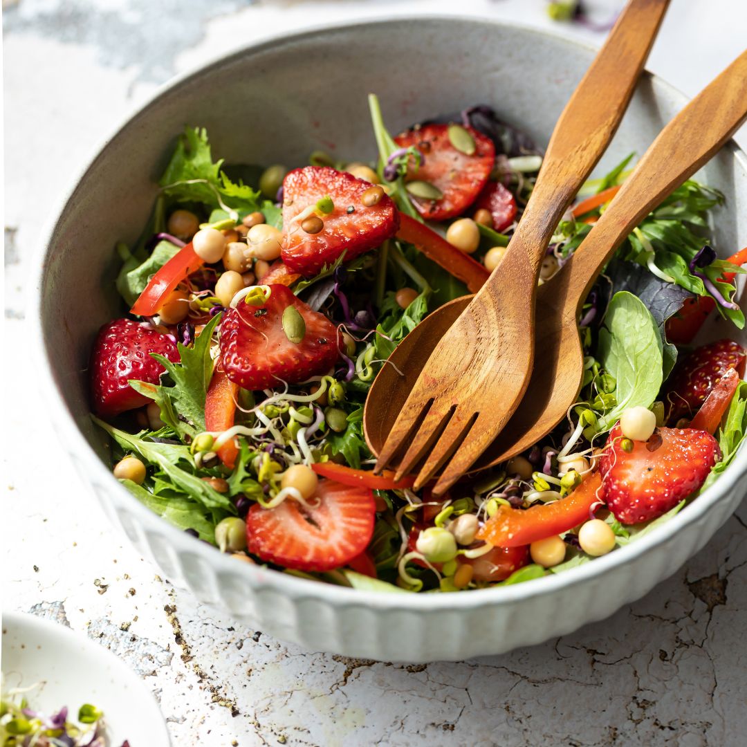 Serving a fresh summer salad with strawberries and greens using a handcrafted teak wood salad server set in a white ceramic bowl.