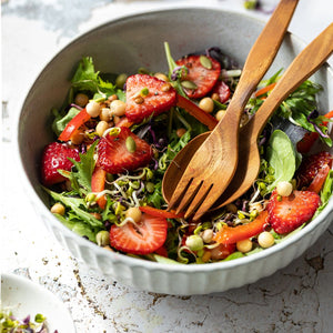 Serving a fresh summer salad with strawberries and greens using a handcrafted teak wood salad server set in a white ceramic bowl.