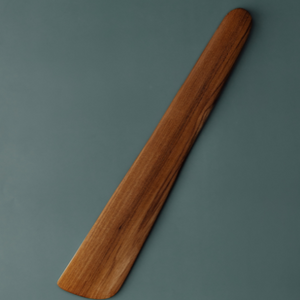 A handcrafted teak wood sauté spatula and scraper featuring a wide, flat-edged blade designed for effortless stirring, flipping, and deglazing. The spatula is carved from a single piece of durable, golden-brown teak wood with a rich natural grain and a smooth, food-safe finish. This long-handled, non-toxic kitchen tool is ideal for use with non-stick cookware and provides an ergonomic grip for everyday cooking in a sustainable, artisanal kitchen.