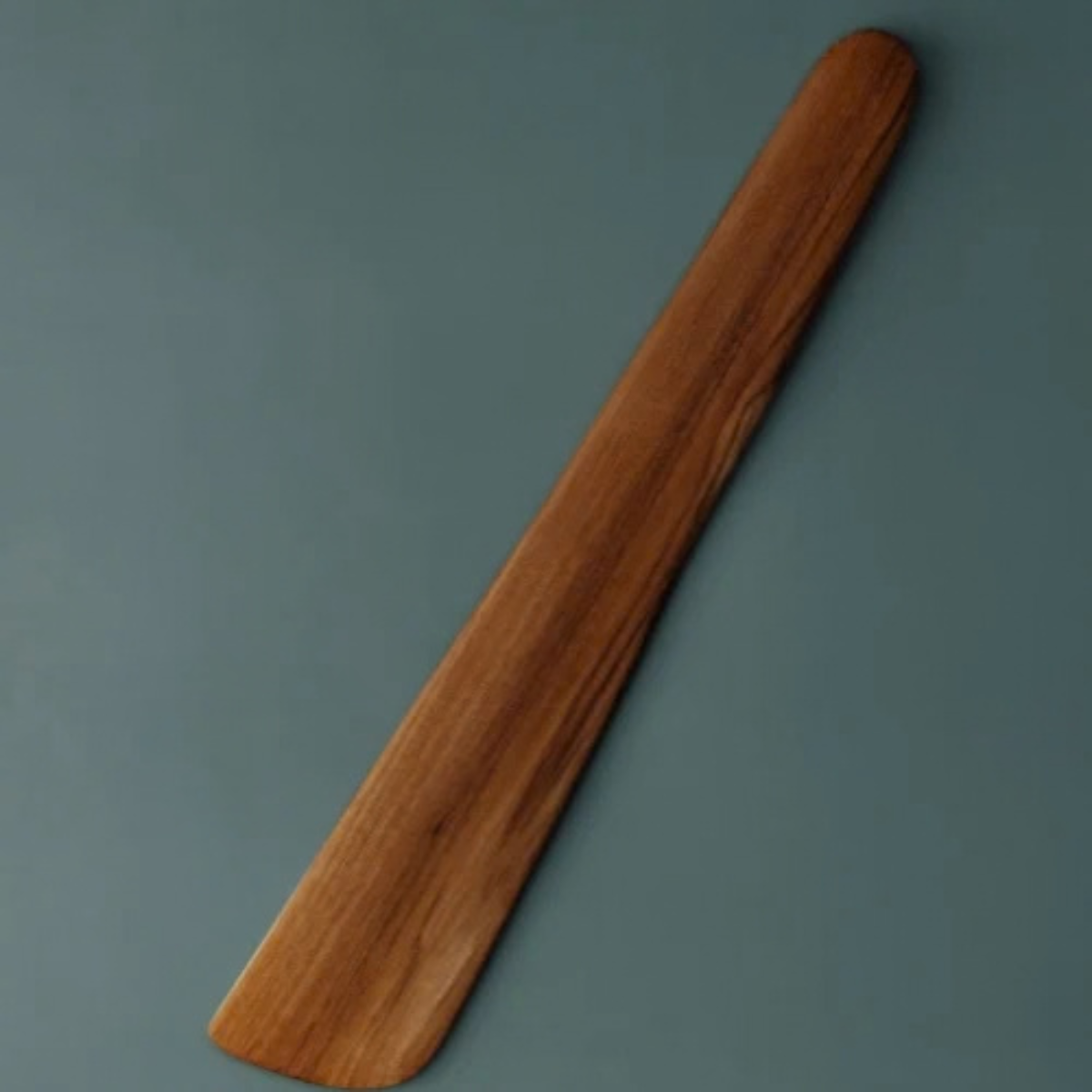 A handcrafted teak wood sauté spatula and scraper featuring a wide, flat-edged blade designed for effortless stirring, flipping, and deglazing. The spatula is carved from a single piece of durable, golden-brown teak wood with a rich natural grain and a smooth, food-safe finish. This long-handled, non-toxic kitchen tool is ideal for use with non-stick cookware and provides an ergonomic grip for everyday cooking in a sustainable, artisanal kitchen.