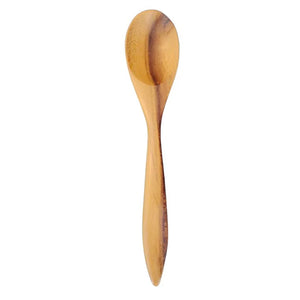 A vertical product photograph of a single handcrafted teak wood teaspoon from a set of four, shown against a crisp white background. The spoon features a unique, ergonomically angled handle and a rounded, shallow head, showcasing the rich, golden-brown natural grain and smooth, food-safe finish of the sustainable teak. Each spoon is carved from a single piece of wood, making this a durable, plastic-free, and non-toxic choice for daily culinary use or as part of an artisan kitchen collection.