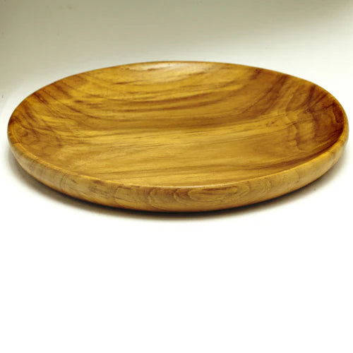 A handcrafted, round teak wood plate or serving platter, 15 cm in diameter isolated on a smooth, dark forest green background. The image showcases the rich, swirling natural wood grain with deep golden-brown and amber tones, highlighting the plate's polished finish and organic, slightly irregular rim. This durable, sustainable wooden dinnerware is ideal for serving appetizers or side dishes.