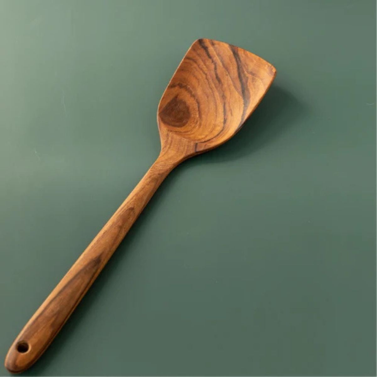A single wooden spatula with a long handle and a square-shaped blade, shown diagonally on a solid dark green background.