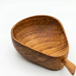 A close-up, high-angle view of a handcrafted, pear-shaped teak wood bowl with rich natural grain patterns and warm reddish-brown tones, featuring a small carved handle at the bottom right, shown against a seamless white background.